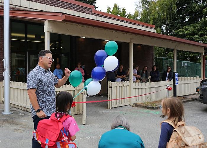 一名男子站在一些氦气球和一根红丝带之间的银支架旁边